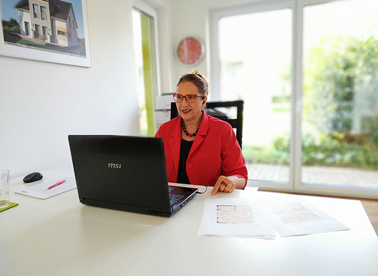 Hausbau mit Frau Fertighaus_Über mich_das Bild zeigt Sophia Maria Wächtersbach am Tisch sitzend mit dem Blick auf einen Laptop Bildschirm