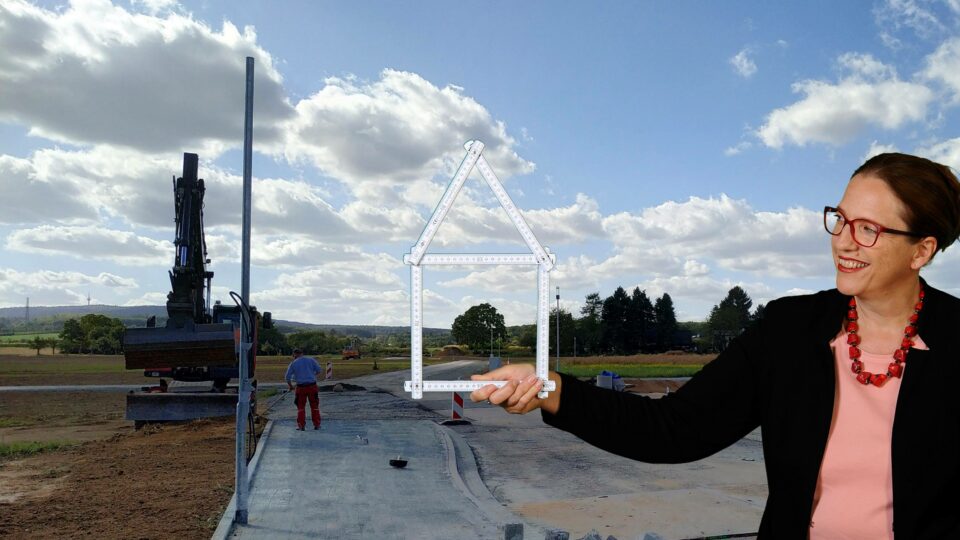 Hausbau mit Frau Fertighaus, über mich, Bild zeigt Sophia Maria Wächtersbach vor einem Neubaugebiet, sie hält einen Zollstock, der zu einem Haus geformt ist