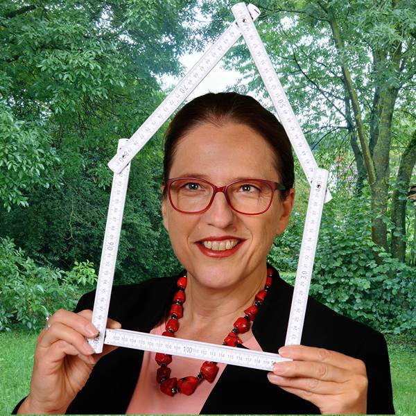 Hausbau mit Frau Fertighaus_das Bild zeigt ein portrait von Sophia Maria Wächtersbach mit einem Zollstock in Hausform vor einem grün bewachsenen Baugrundstück