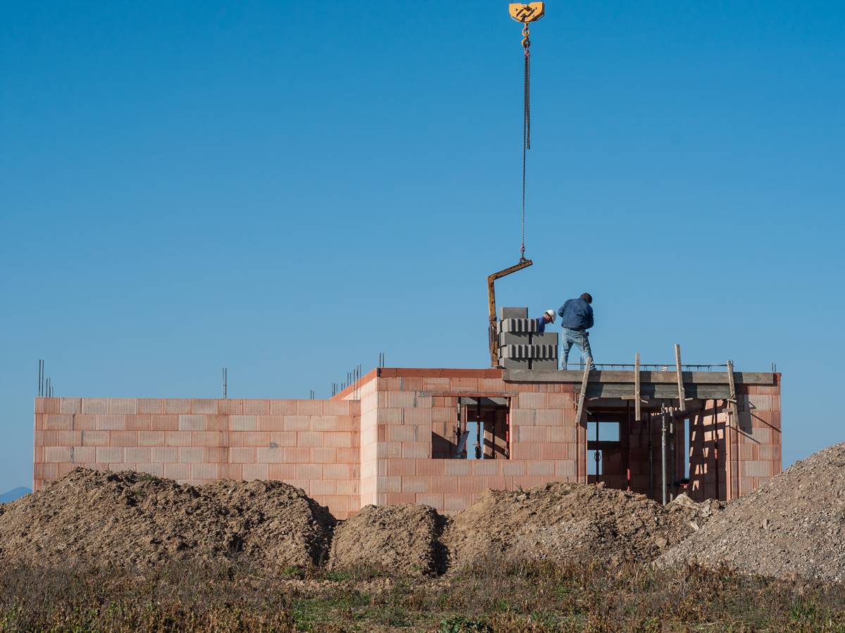 Bild zeigt einen Massivhaus Rohbau aus Ziegelstein, das Erdgeschoss ist gemauert, ein Bauarbeiter steht auf der Zwischendecke, im Vordergrund Erde, im Hintergrund blauer Himmel, Blog Frau Fertighaus