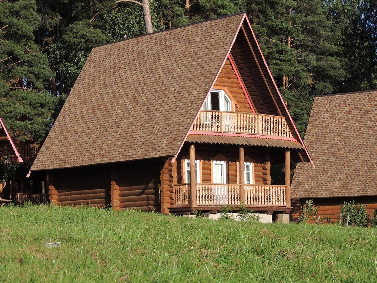 Bild zeigt älteres Holzhaus mit Satteldach und Balkonen an der Giebelseite, Wald im Hintergrund, Blog Frau Fertighaus