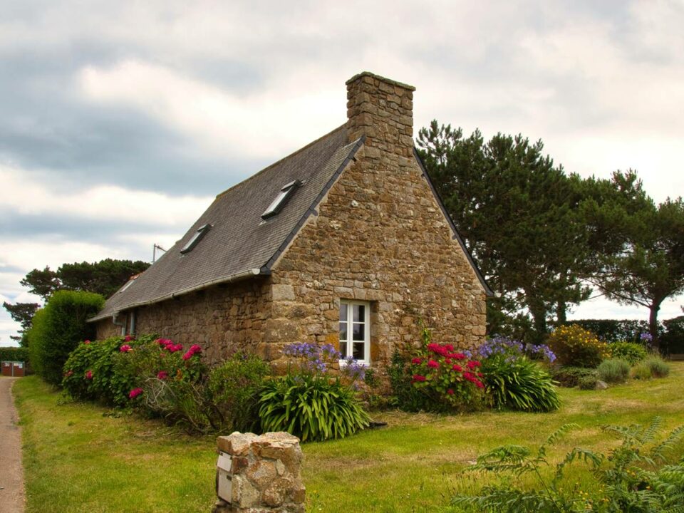 Bild zeigt ländliches Bruchsteinhaus mit Satteldach und Schornstein, umgeben von hübsch angelegtem Blumengarten, Blog Frau Fertighaus, Beitrag: Fertighaus oder Massivhaus - was ist besser