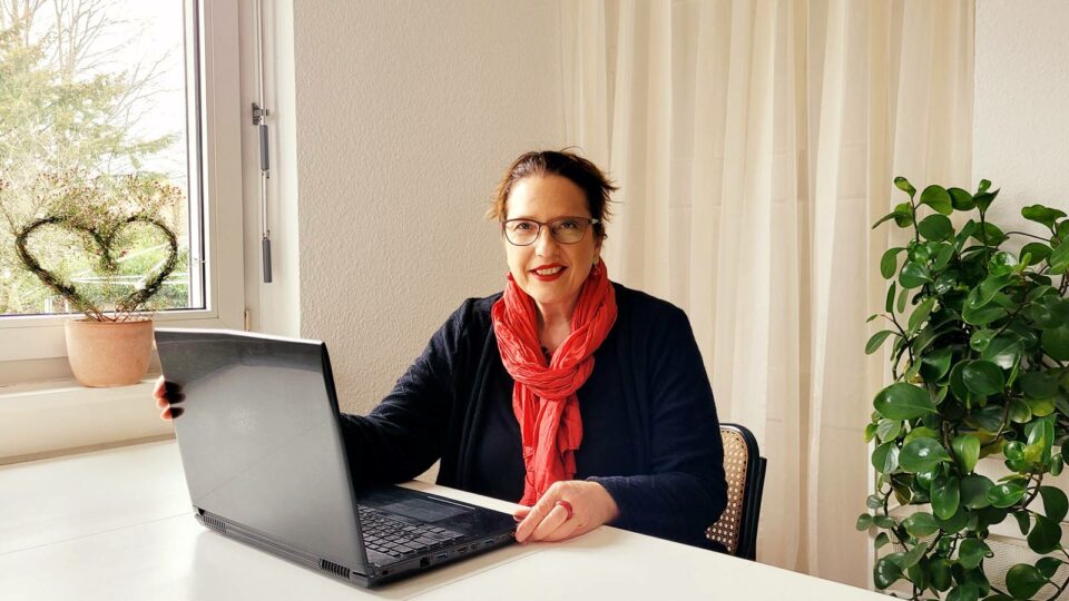 Das Bild zeigt Sophia Maria Wächtersbach an einem Laptop sitzend. Sie schaut auf und lächelt dich an.